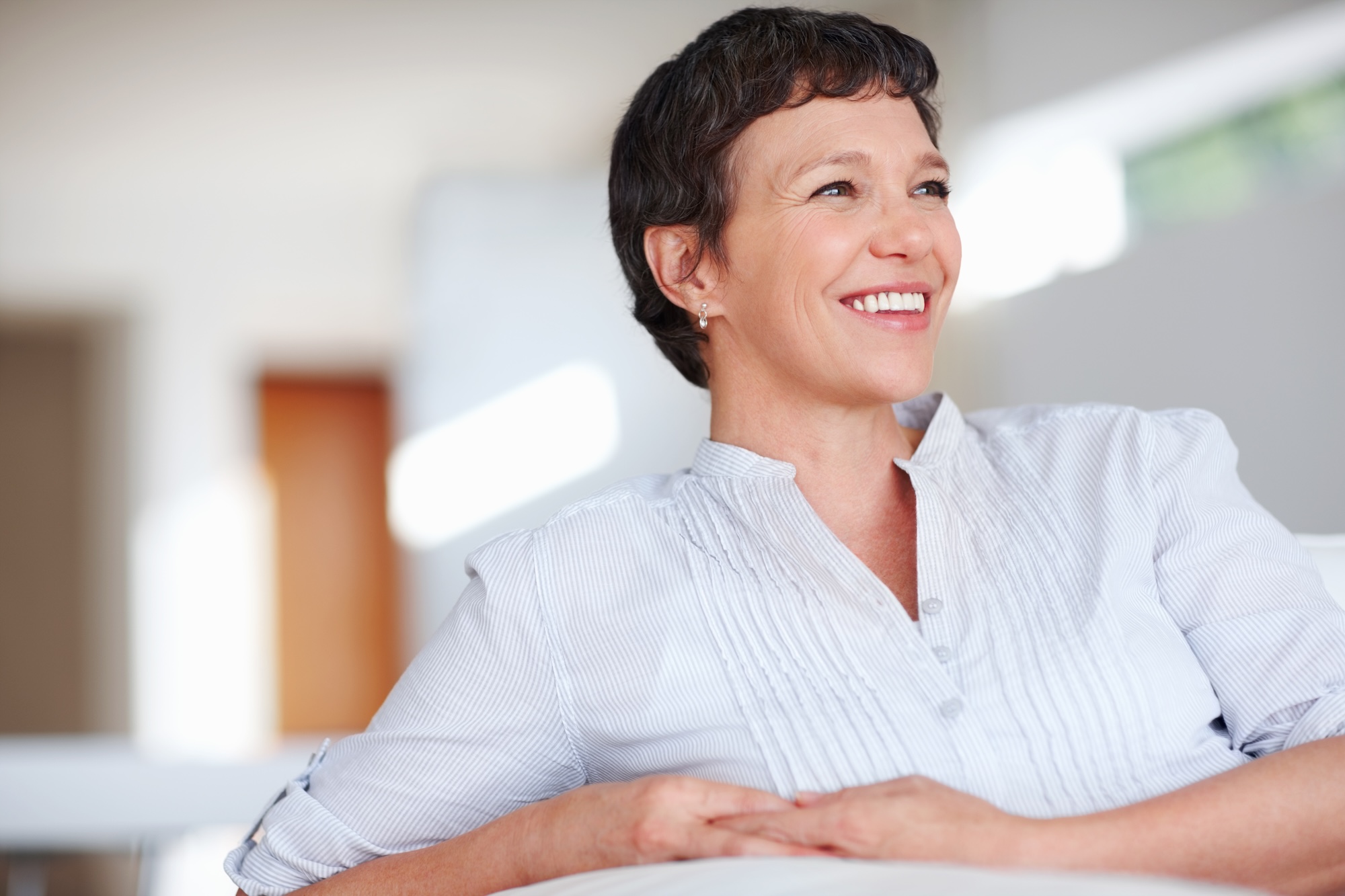 Beautiful brunette woman sitting on couch with a smile after going to Vive Aesthetics & Wellness for a Botox brow lift near Evesham, NJ.