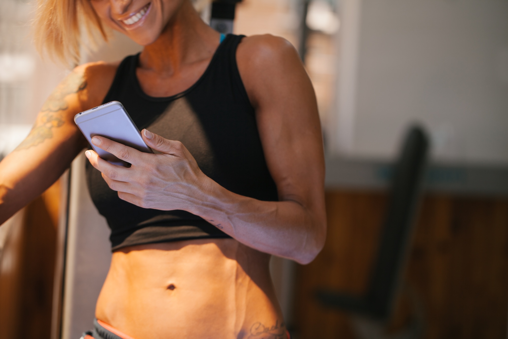 Woman looking at her phone during a workout break to learn more about Emsculpt near Cherry Hill, NJ.
